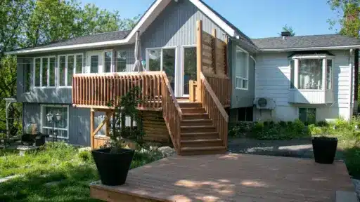 Wooden deck and staircase leading to a modern house with large windows and lush greenery