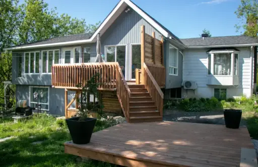 Wooden deck and staircase leading to a modern house with large windows and lush greenery