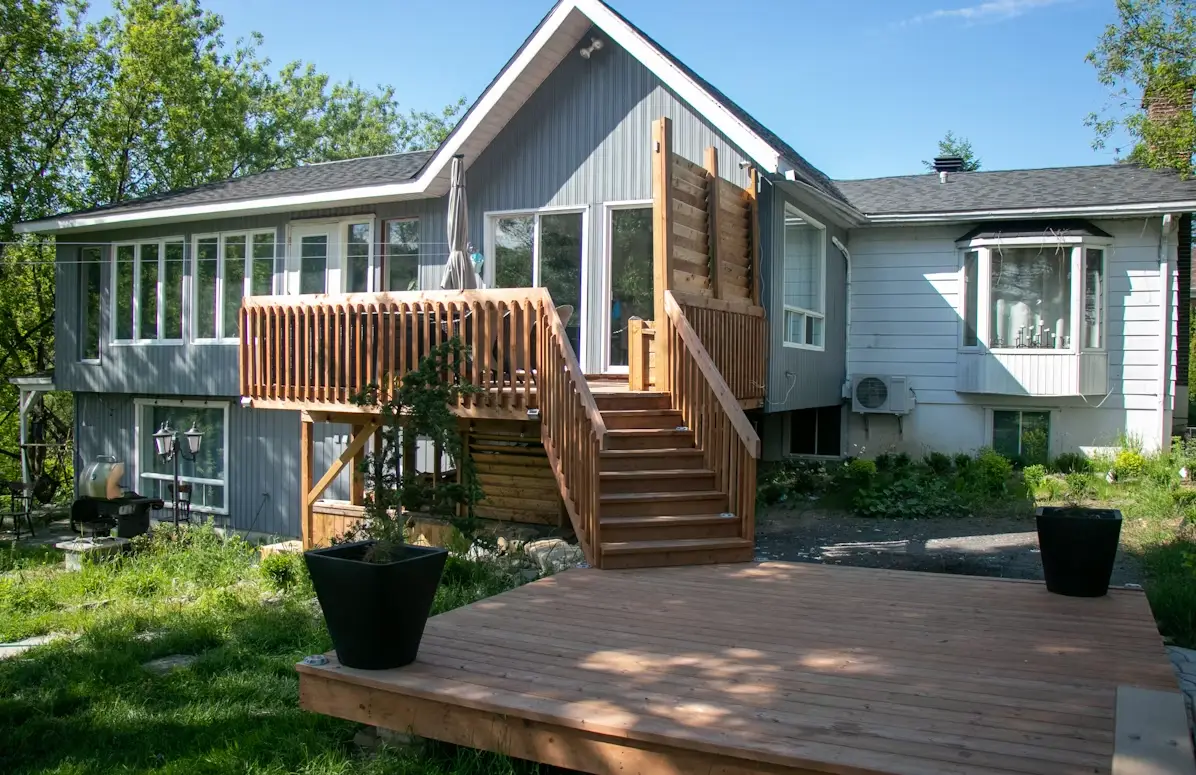Wooden deck and staircase leading to a modern house with large windows and lush greenery