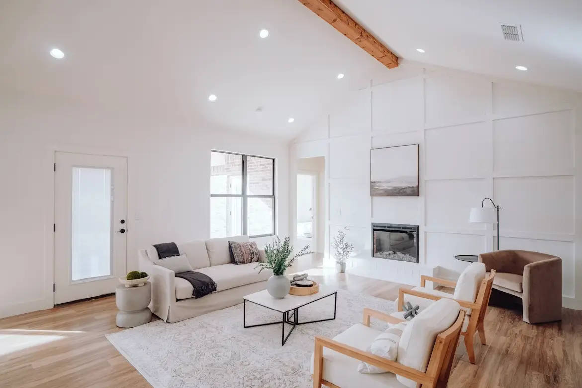 Modern living room with neutral sofa, armchairs, and coffee table under vaulted ceiling with wood beam