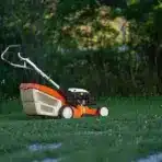 Orange and black lawnmower on grass in a lush garden setting