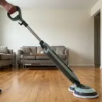 a man mopping a hardwood floor with a green and grey steam mop in a bright living room