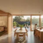Modern open-plan kitchen and living area with sunlight, large windows, and two people at the counter