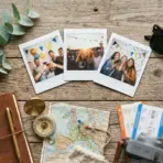 travel themed flat lay with leaves, sunglasses, photos, journal, map, passport, tickets, compass, and camera on a wooden table
