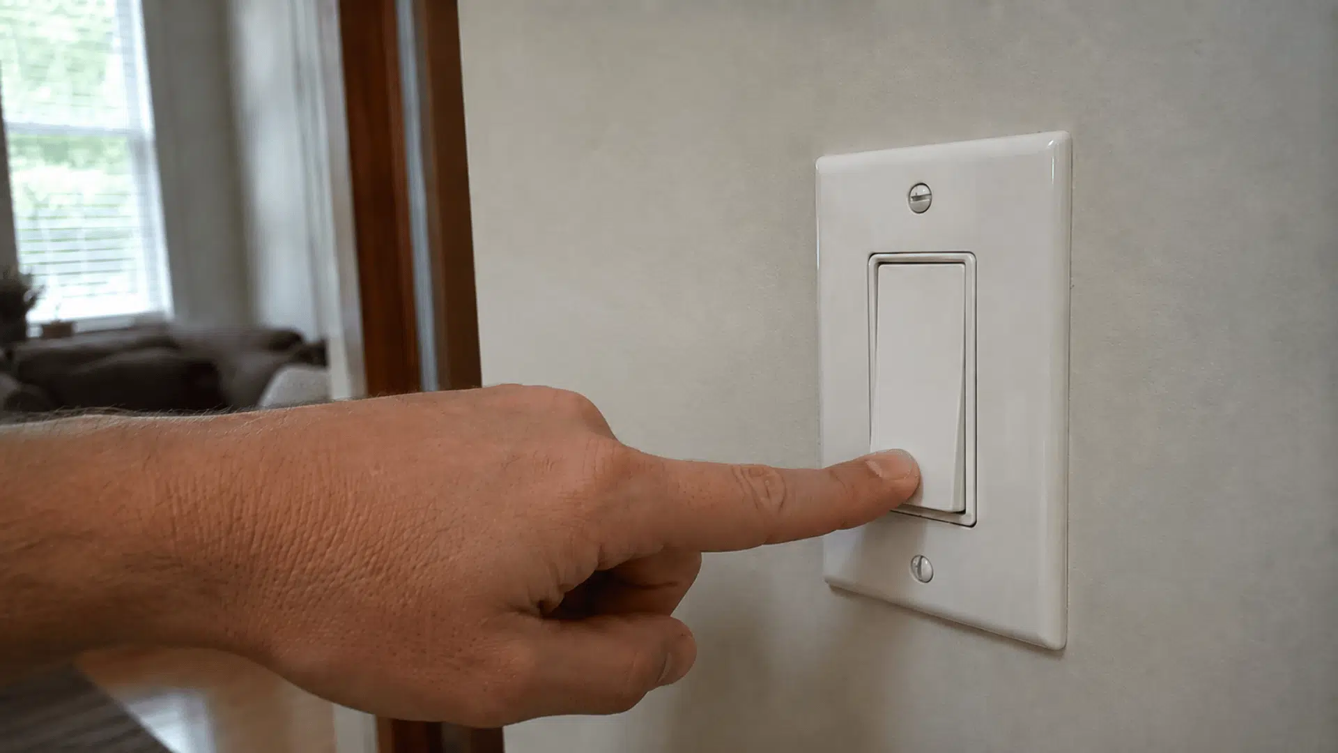 hand pressing a wall light switch off to reduce unnecessary heat from lights inside the room