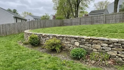 a curved gravity retaining wall made of stacked natural stone along a residential backyard slope