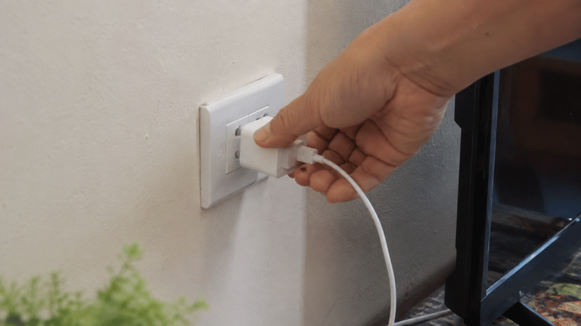 hand unplugging a charger from a wall outlet to reduce standby power use and unnecessary indoor heat