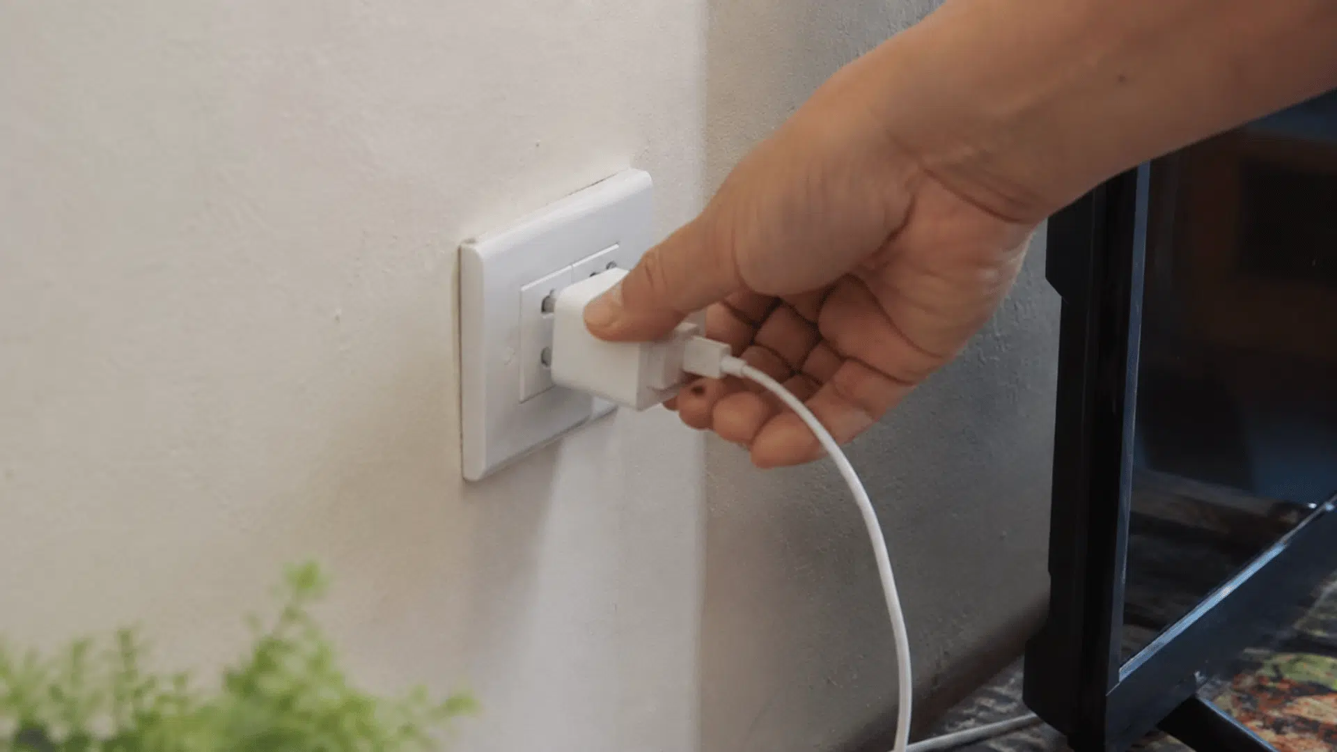 hand unplugging a charger from a wall outlet to reduce standby power use and unnecessary indoor heat