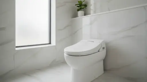 Modern white toilet in bright marble-tiled bathroom with frosted window and small potted plant