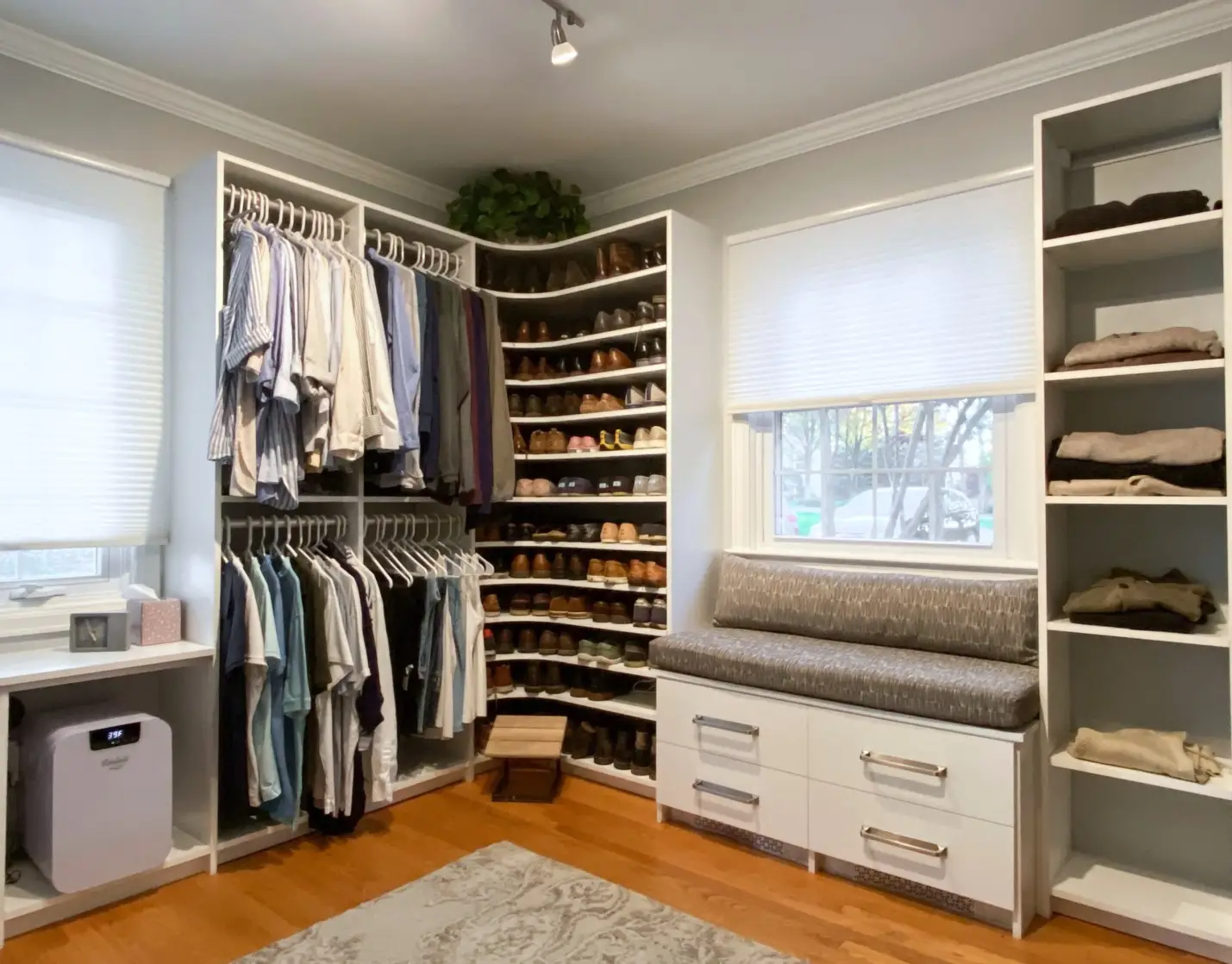 Organized walk-in closet with clothes, shoes, bench seating, and storage shelves in bright room