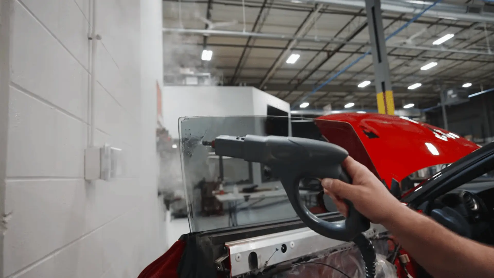 a technician inspects the exposed inner panel of a red car door inside a brightly lit automotive workshop