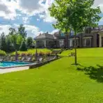Luxurious brick house with pool and manicured lawn under blue sky