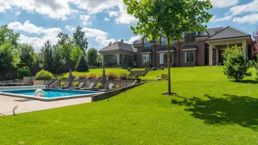 Luxurious brick house with pool and manicured lawn under blue sky