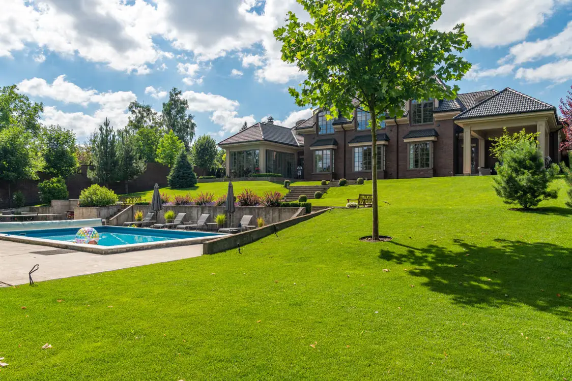 Luxurious brick house with pool and manicured lawn under blue sky