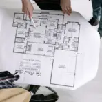 Hands pointing at architectural floor plan on large paper in brightly lit room
