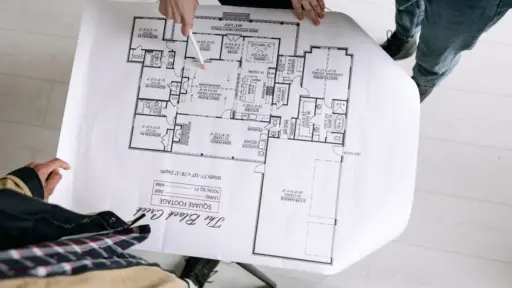 Hands pointing at architectural floor plan on large paper in brightly lit room