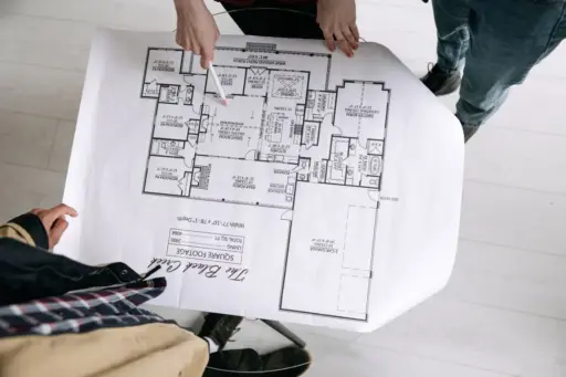 Hands pointing at architectural floor plan on large paper in brightly lit room