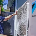 Man examining outdoor air conditioning unit in a sunny backyard setting