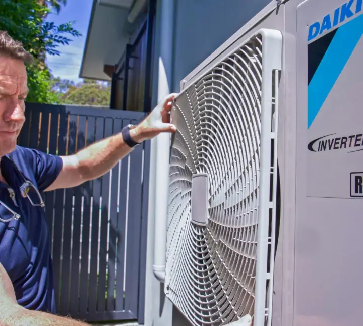 Man examining outdoor air conditioning unit in a sunny backyard setting