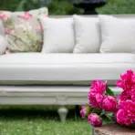 Elegant outdoor patio scene with white sofa, floral cushion, and vibrant pink peonies in foreground