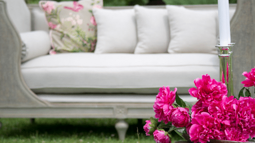 Elegant outdoor patio scene with white sofa, floral cushion, and vibrant pink peonies in foreground