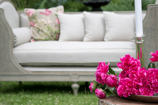 Elegant outdoor patio scene with white sofa, floral cushion, and vibrant pink peonies in foreground