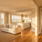 Bright living room and kitchen with beige sofa, wicker basket, and wooden floors under natural light