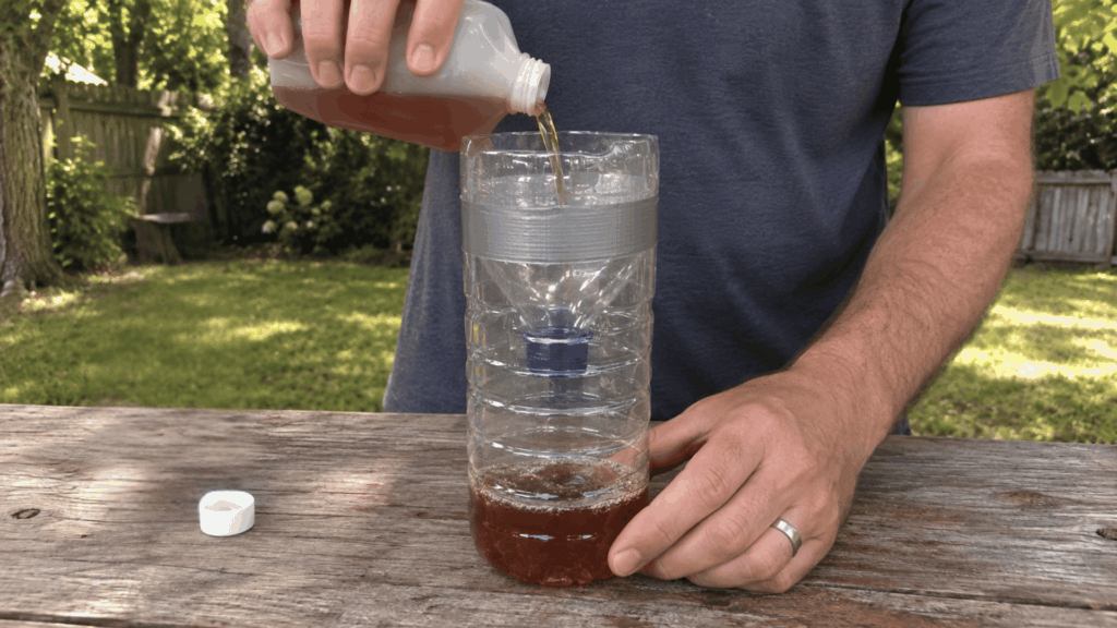 pouring brown liquid bait into a homemade plastic bottle wasp trap on an outdoor table