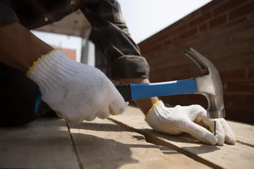 Person in white gloves hammering nail into wooden plank outdoors