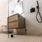 Modern bathroom with floating wood vanity, black fixtures, and glass shower partition