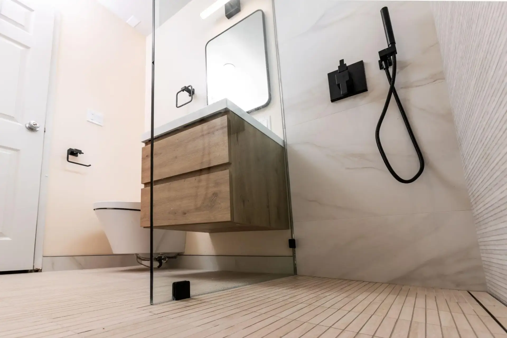 Modern bathroom with floating wood vanity, black fixtures, and glass shower partition