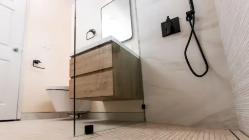 Modern bathroom with floating wood vanity, black fixtures, and glass shower partition