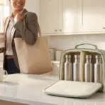 Person holding coffee and tote bag in modern kitchen with insulated bag and stainless steel bottles