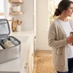 Woman holding travel mug in bright kitchen with open insulated lunch bag on counter