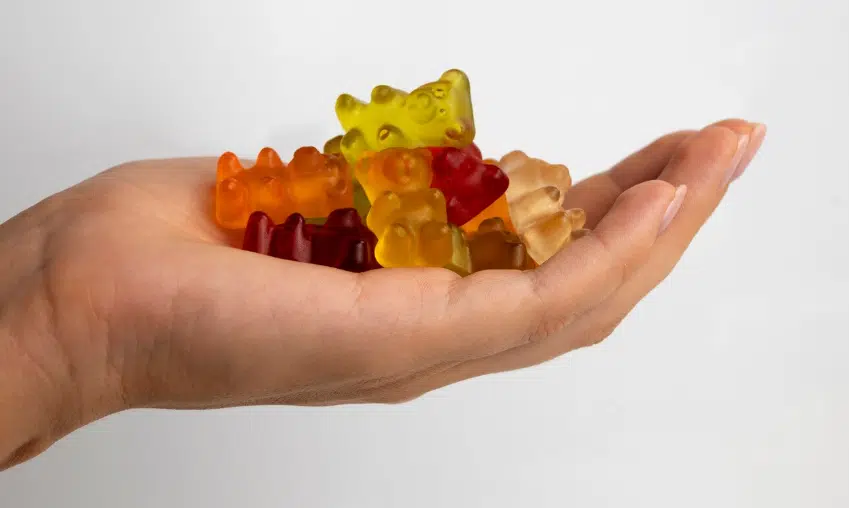Hand holding colorful gummy bears against a plain white background