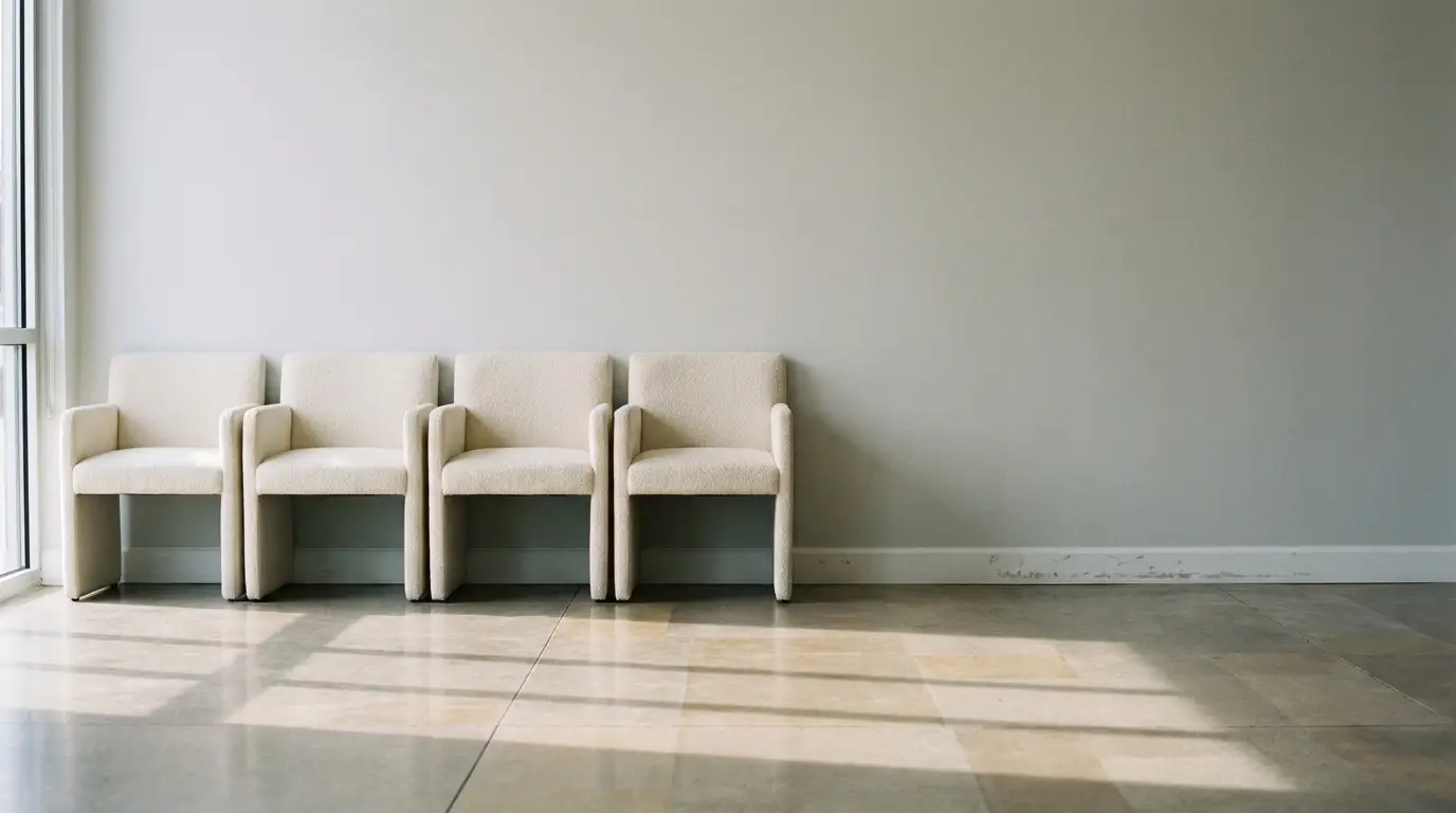 Four beige chairs against a light gray wall in a sunlit room with tiled floor