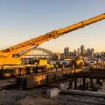 Construction site with large yellow crane and workers against city skyline at sunset
