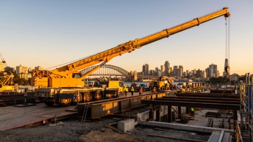 Construction site with large yellow crane and workers against city skyline at sunset