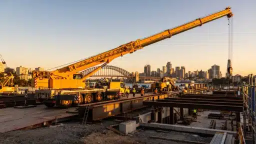 Construction site with large yellow crane and workers against city skyline at sunset