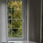 White-framed window with sheer curtains overlooking lush green trees