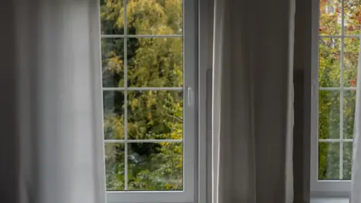 White-framed window with sheer curtains overlooking lush green trees