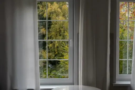 White-framed window with sheer curtains overlooking lush green trees