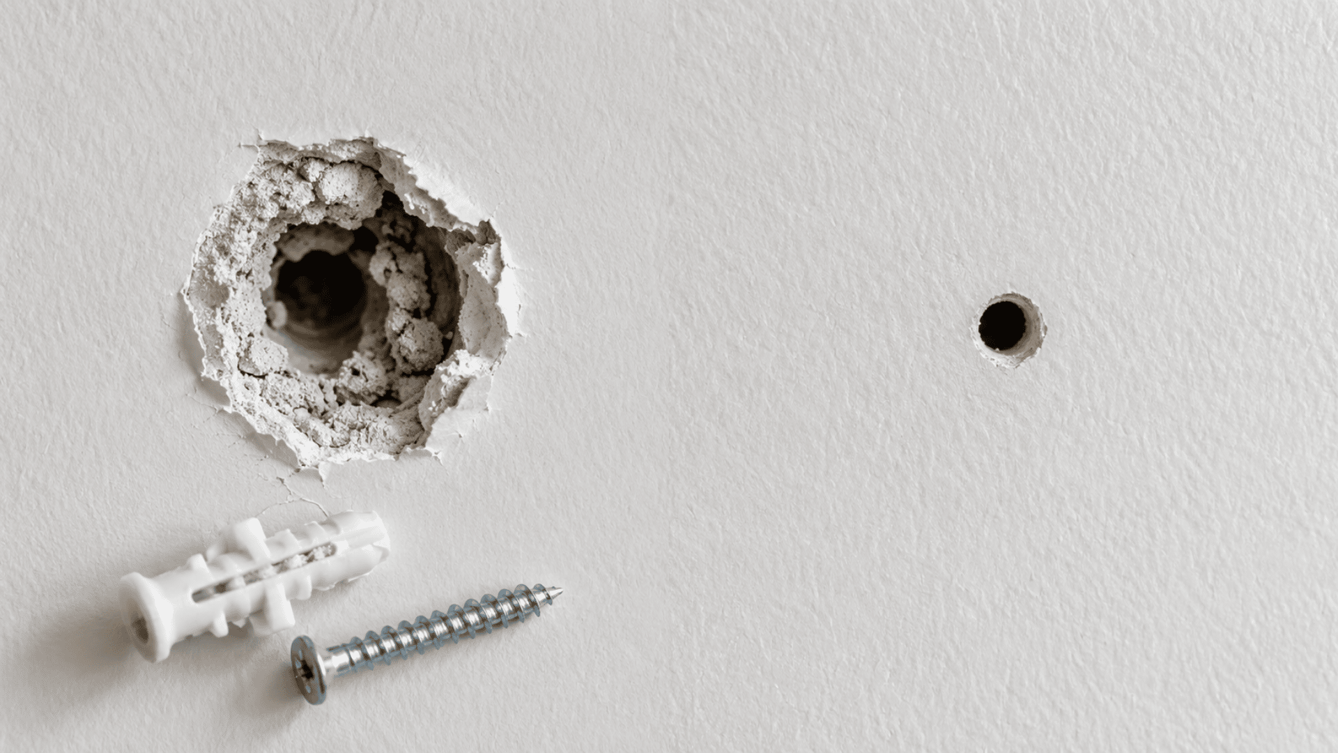 enlarged damaged drywall hole with a loose anchor beside a new mounting point in intact drywall