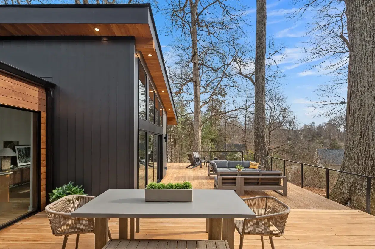 Modern outdoor deck with black exterior, wooden furniture, and trees in the background