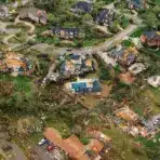 Aerial view of tornado-damaged suburban homes and debris scattered across neighborhood streets.