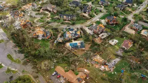Aerial view of tornado-damaged suburban homes and debris scattered across neighborhood streets.