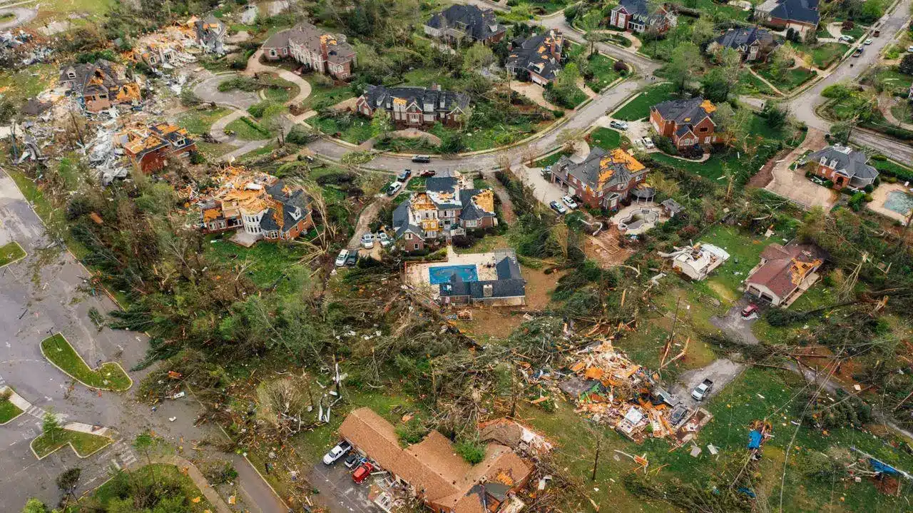Aerial view of tornado-damaged suburban homes and debris scattered across neighborhood streets.
