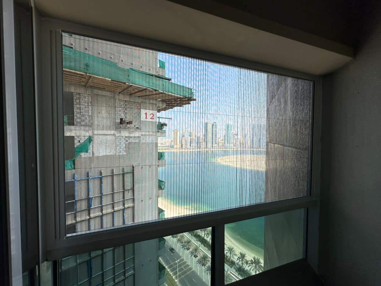 Construction site viewed through window with city skyline and waterfront in the background