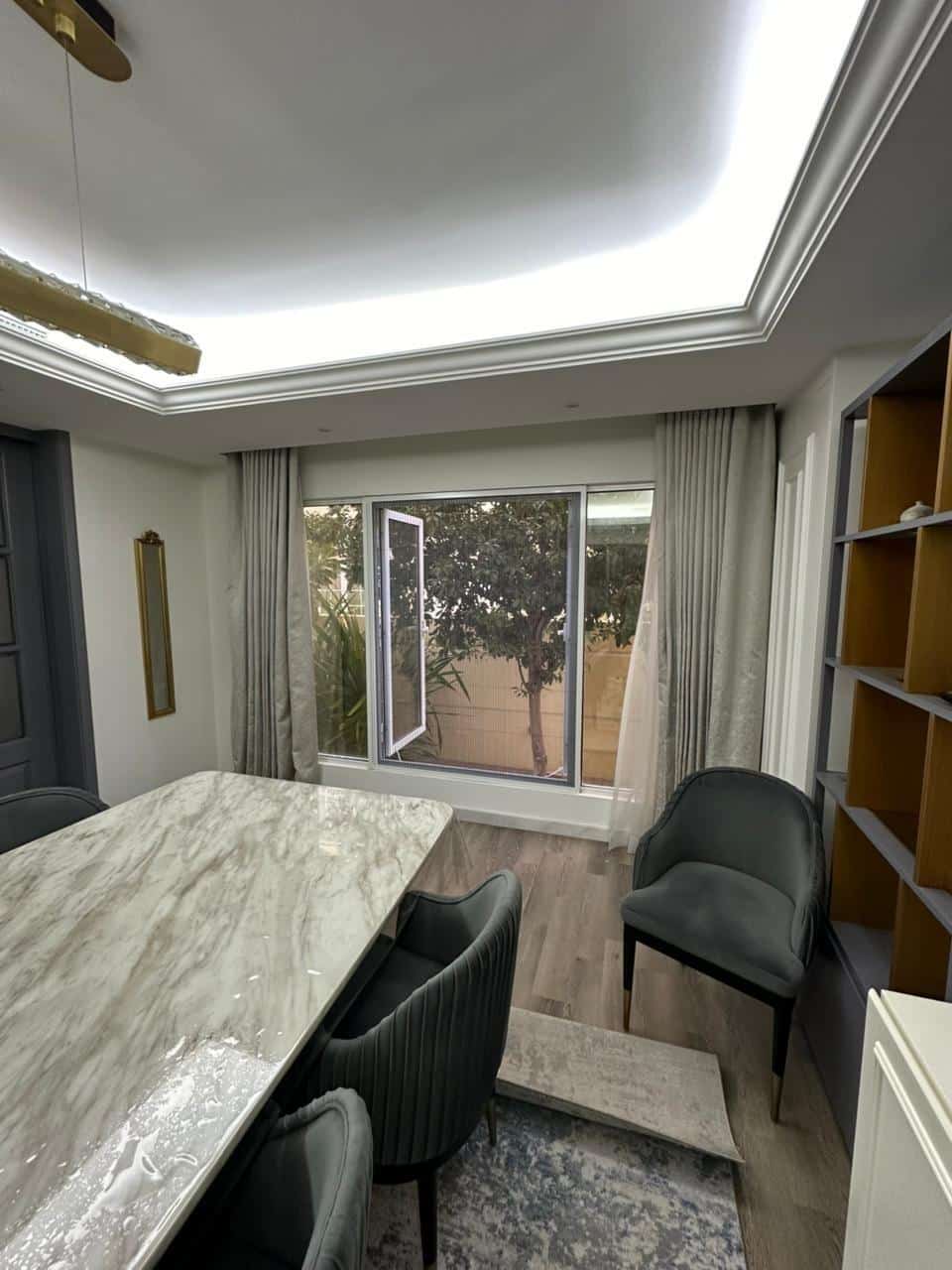 Marble dining table with gray chairs in a modern room with large window and open drapes