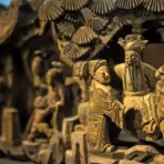 Ornate wooden sculpture depicting figures in traditional attire with intricate carvings and fine details